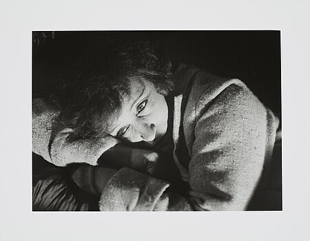 Eine schwarz-weiß Fotografie eine Frau deren Kopf auf ihren verschränkten Armen ruht.