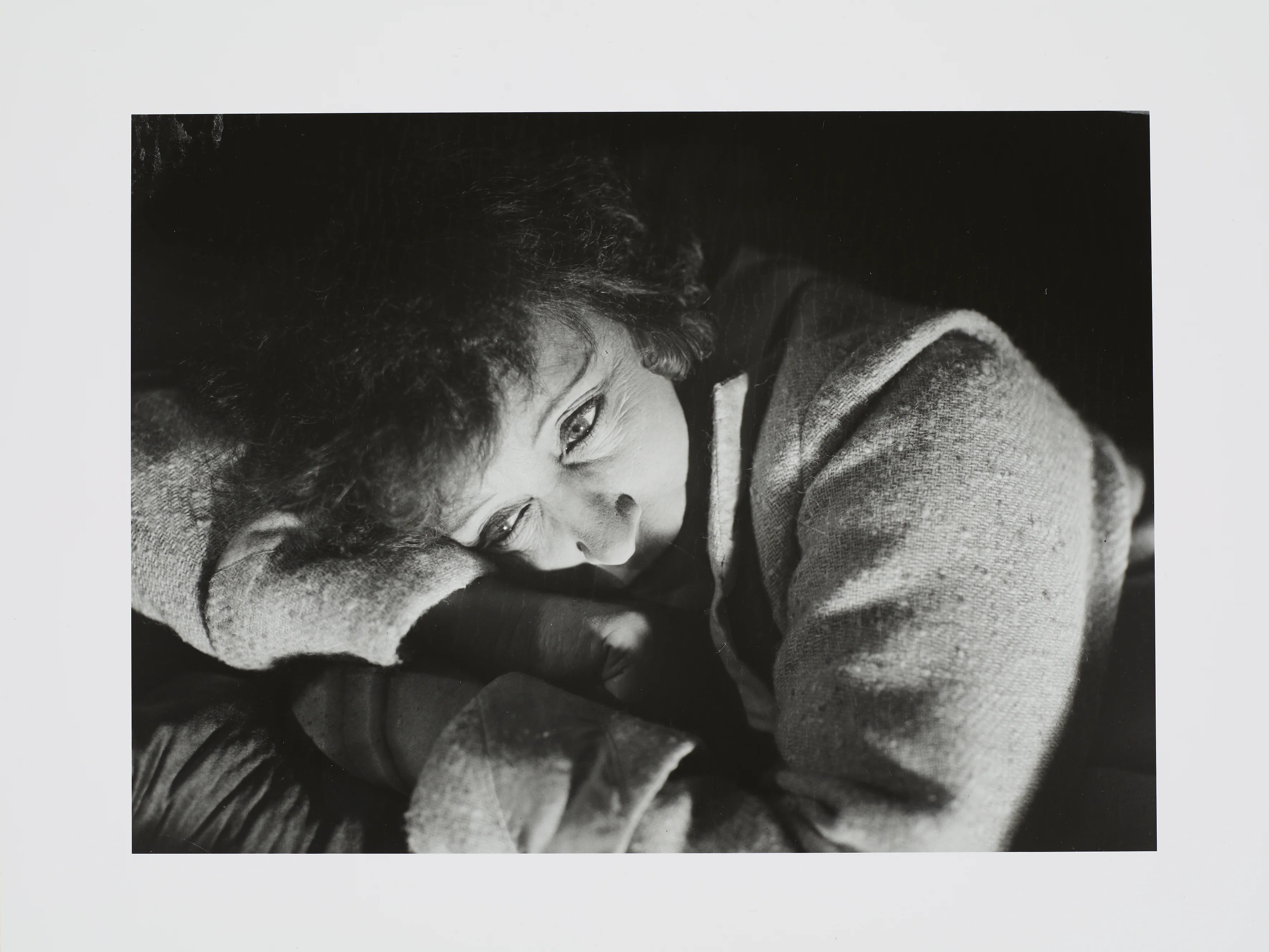 Eine schwarz-weiß Fotografie eine Frau deren Kopf auf ihren verschränkten Armen ruht.