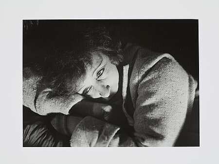 Eine schwarz-weiß Fotografie eine Frau deren Kopf auf ihren verschränkten Armen ruht.
