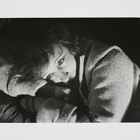 Eine schwarz-weiß Fotografie eine Frau deren Kopf auf ihren verschränkten Armen ruht.