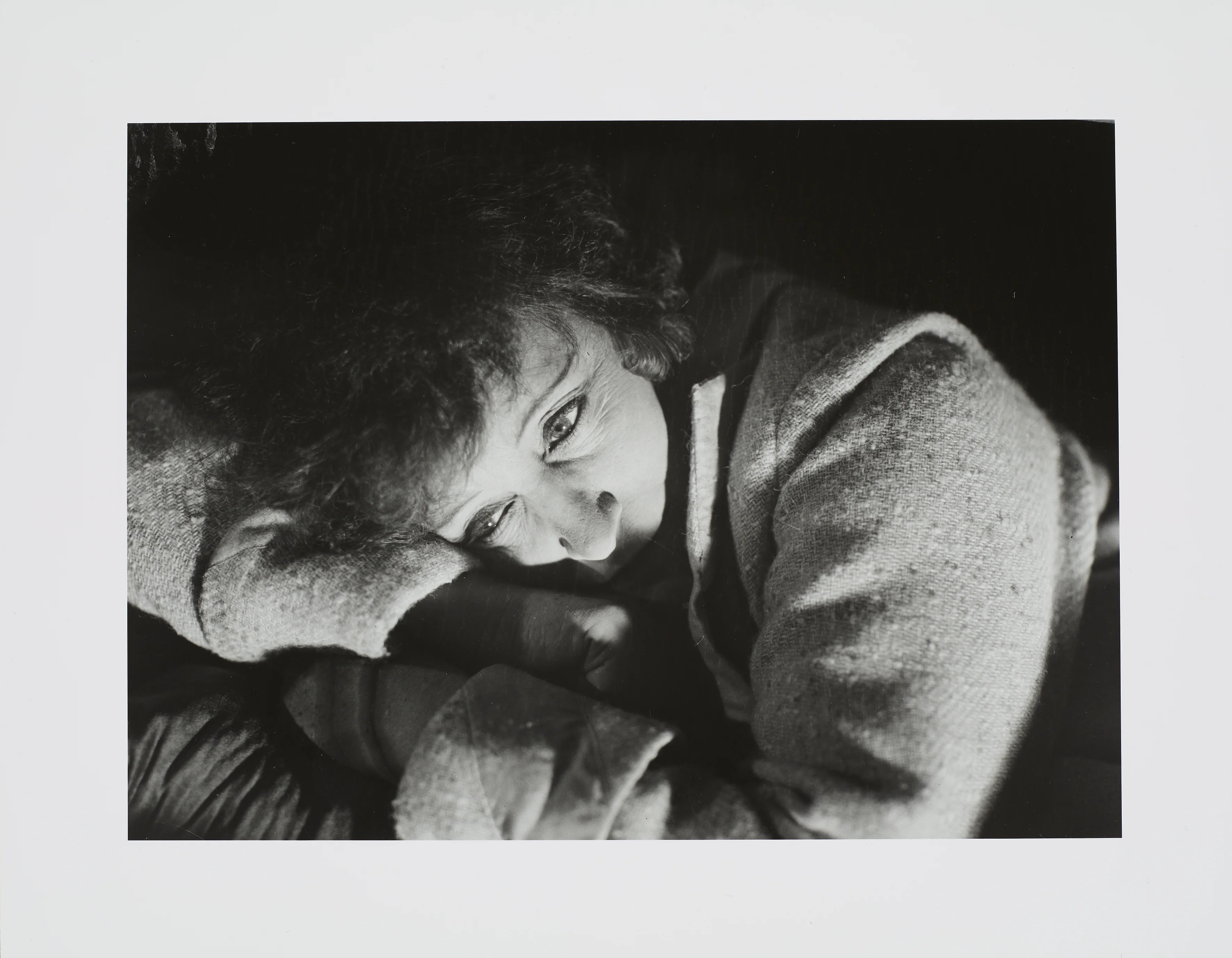 Eine schwarz-weiß Fotografie eine Frau deren Kopf auf ihren verschränkten Armen ruht.